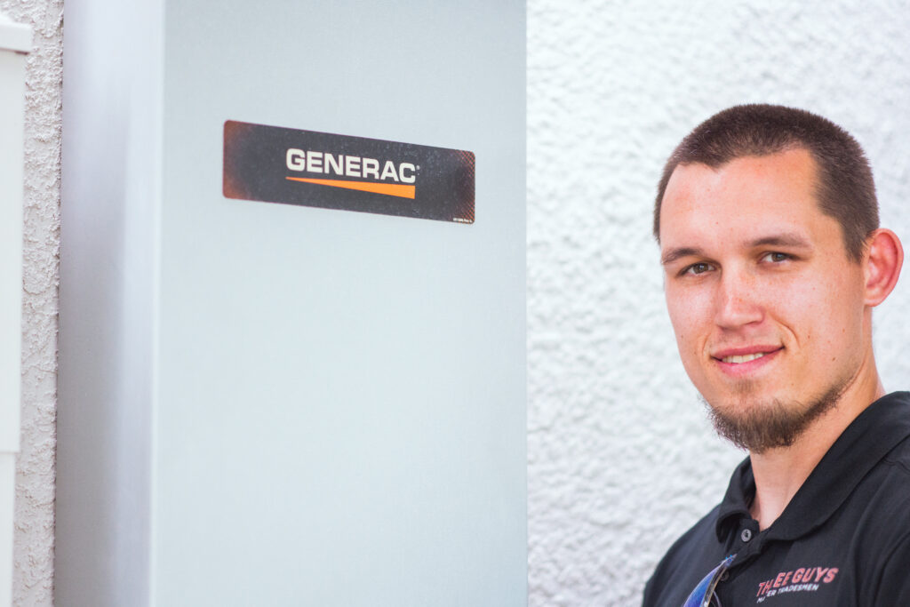 Three Guys Master Tradesmen technician standing beside a Generac transfer switch during a residential generator service visit