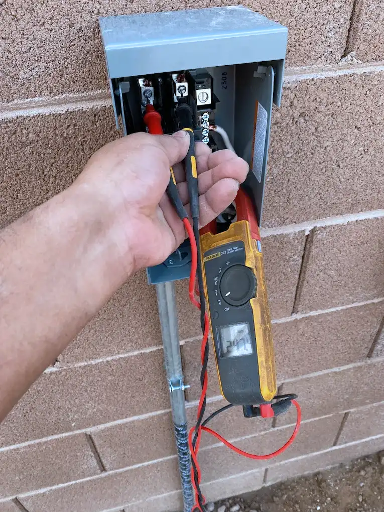 Electrician testing voltage at a pool electrical disconnect box with a clamp meter