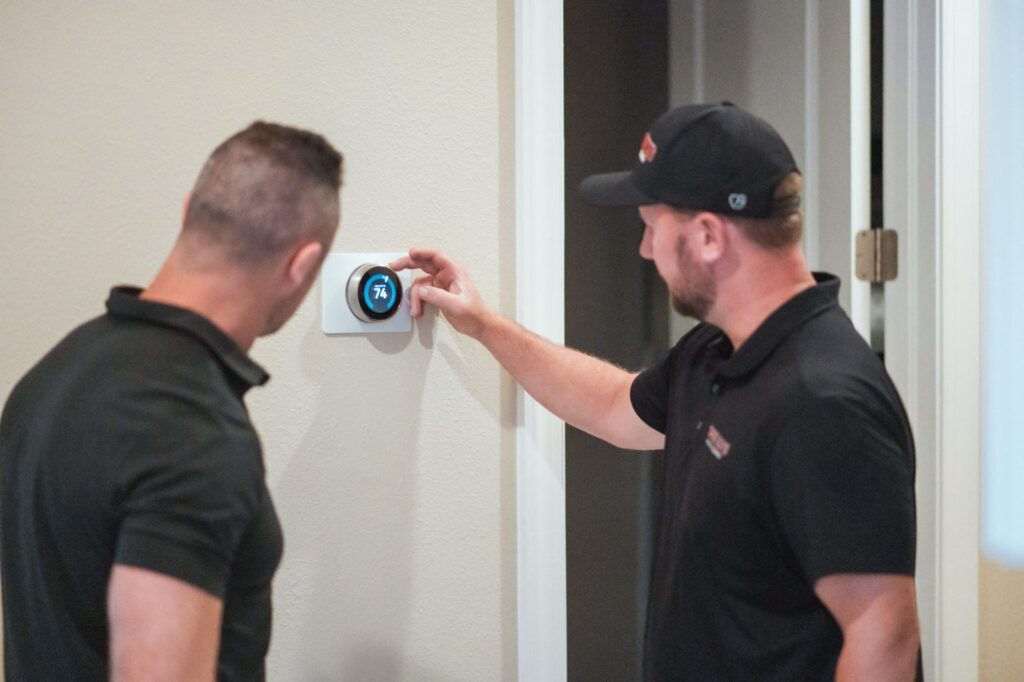 Three Guys Master Tradesmen HVAC technician adjusting a smart thermostat for a homeowner