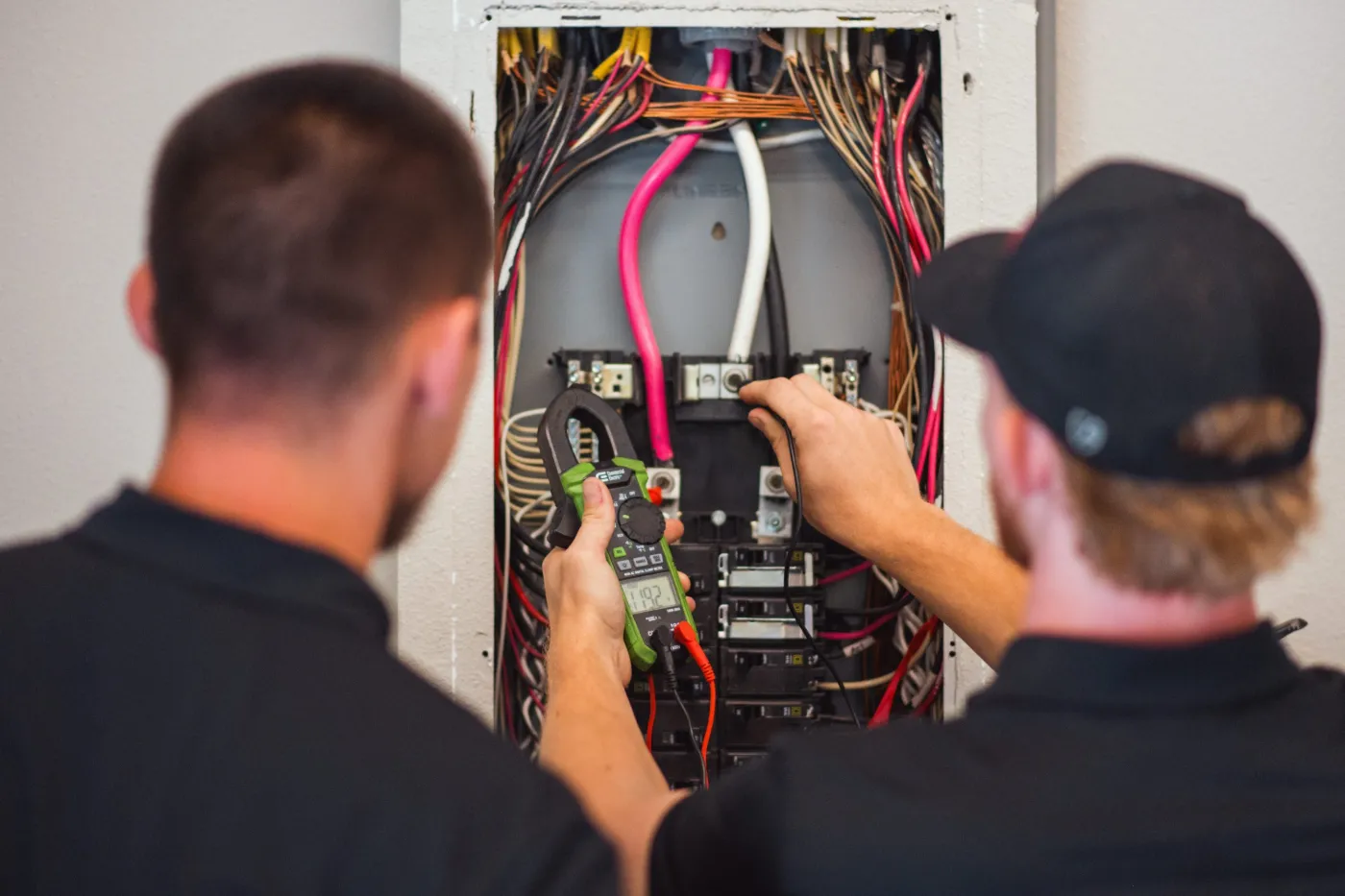 Two Three Guys electricians testing an electrical panel with a clamp meter